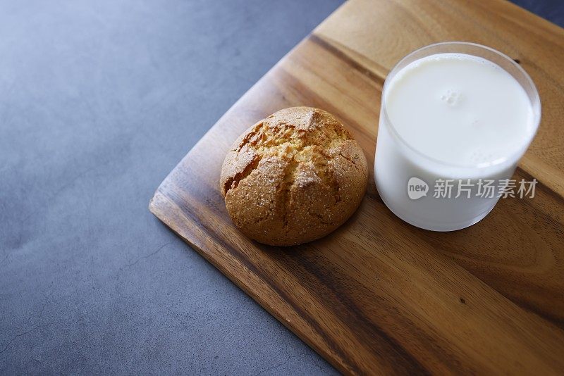 一块橙色的大圆饼干和一杯牛奶放在一块木头砧板上，背景是深灰色的石头