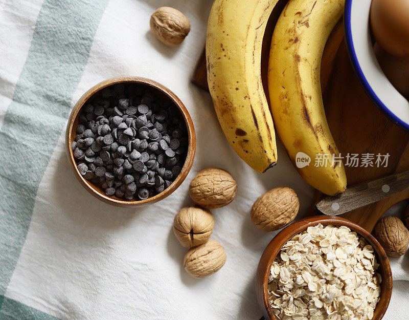 燕麦片和巧克力滴在木盘子上，白色的布上有绿色条纹，香蕉和核桃，特写