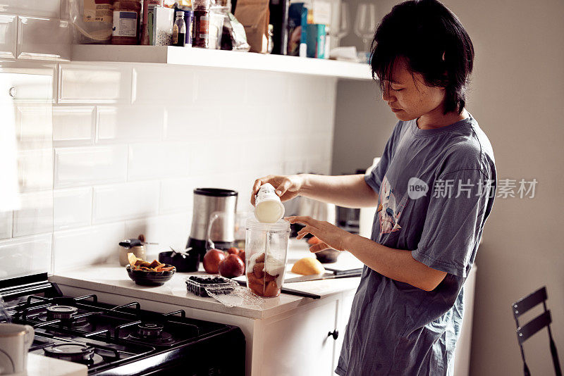 这是一名年轻女子在自家厨房将酸奶倒入容器中制作奶昔的照片