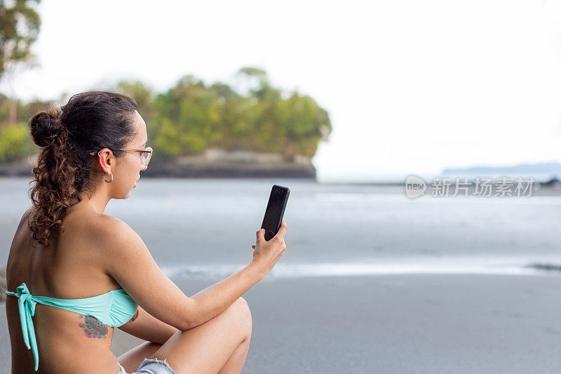 一名成功的年轻女子在海滩上用手机在线购买应用程序
