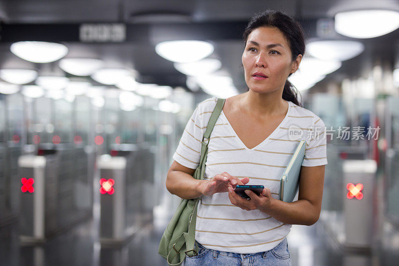 一个女人拿着智能手机站在地铁站里