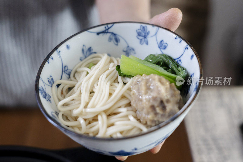 手捧一碗面条，用叶菜和肉丸煮熟