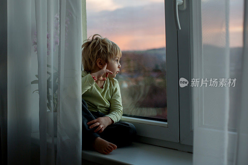 一个蹒跚学步的孩子，坐在夕阳下的窗户上，看着外面