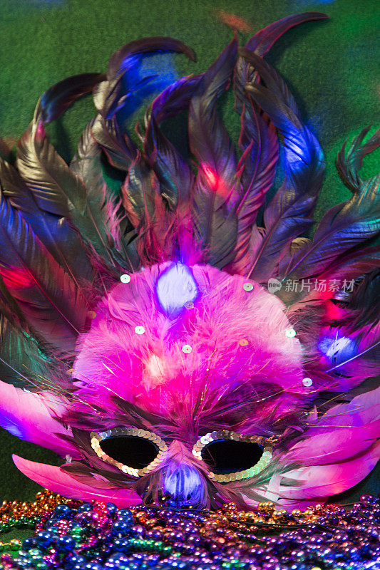 LV狂欢节上的亮片面具，用羽毛装饰在铺有羽毛的床上。彩色的珠子和聚光灯的颜色。