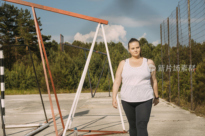 一名超重的女性正准备在户外篮球场上进行日常锻炼