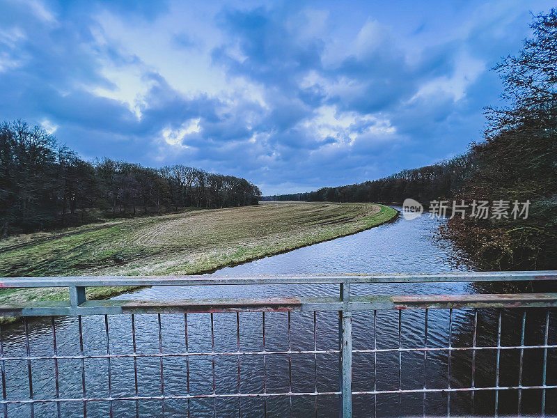 在德国，从一座桥上看到的河流被称为“Gro?e Aa”，旁边是一片田野和一片森林。