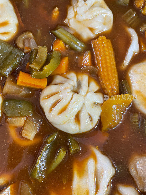 一碗Momos(南亚饺子)的全框图像，白面粉和水面团填充鸡肉和混合蔬菜在肉汤与甜玉米，青椒，胡萝卜丁，细豆类，芹菜和洋葱上升的观点