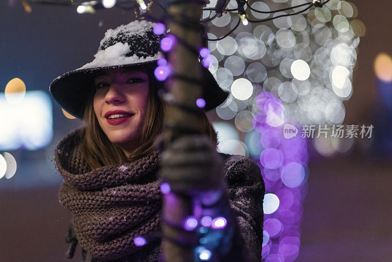 小女孩站在圣诞树前的彩灯下，雪花飘落，漫天飞舞