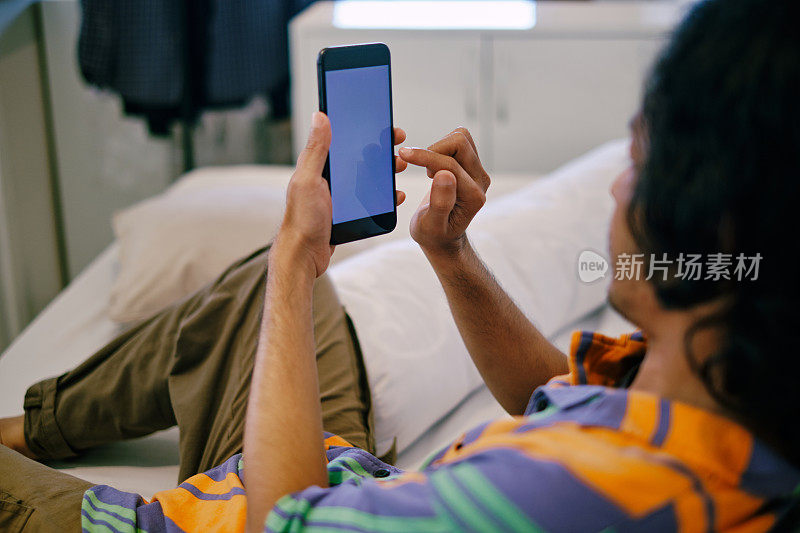 年轻人躺在家里的床上玩智能手机