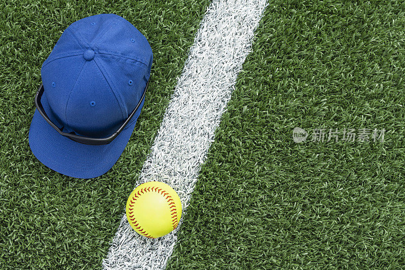 戴着棒球帽和墨镜俯视着一个垒球坐在白色的底线上