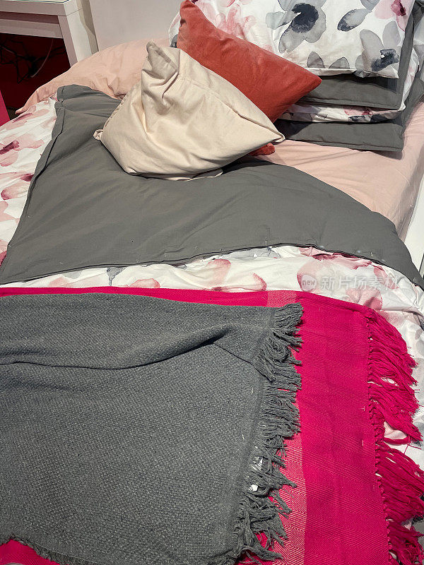 国内卧室的单人床，粉色和灰色的床上用品，皱皱的羽绒被，散落的靠垫，毛毯，室内卧室设计