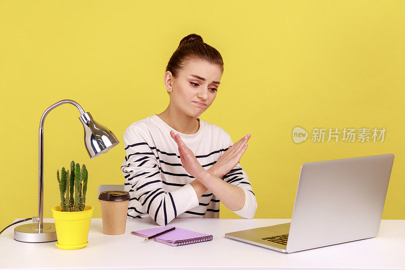 女人坐在工作场所，双手交叉，露出x形，皱着眉头看着笔记本电脑屏幕