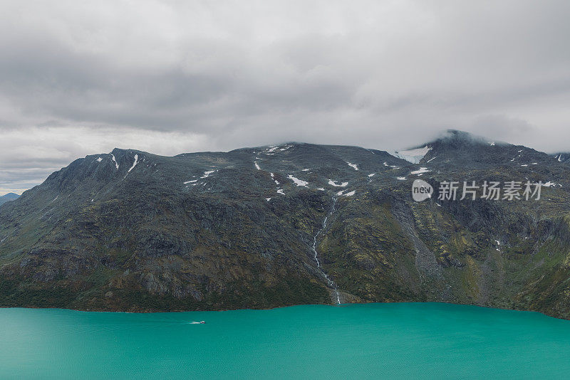 在挪威约顿海门国家公园水晶蓝色的冰川湖上航行的渡轮的戏剧性视图