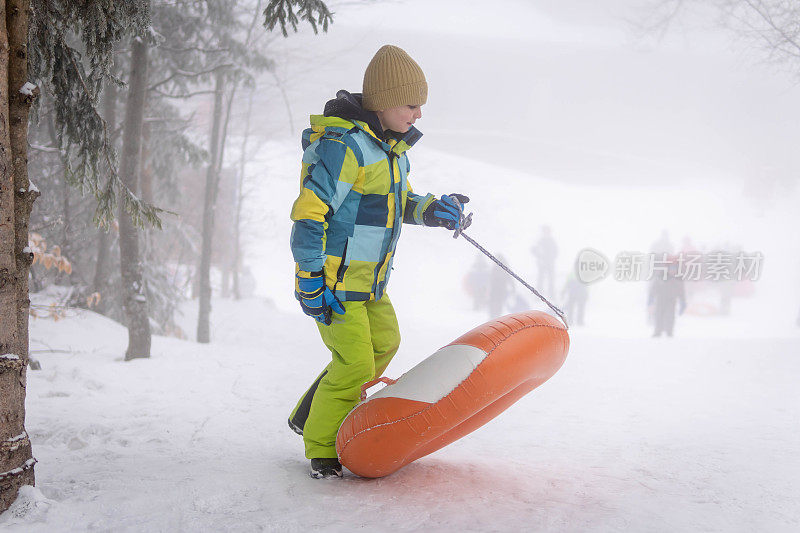 小男孩在雪管上从山上滑下来。