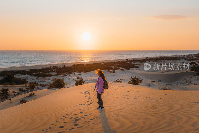 在土耳其海边的沙丘上，背着背包的女人凝视着风景优美的日落