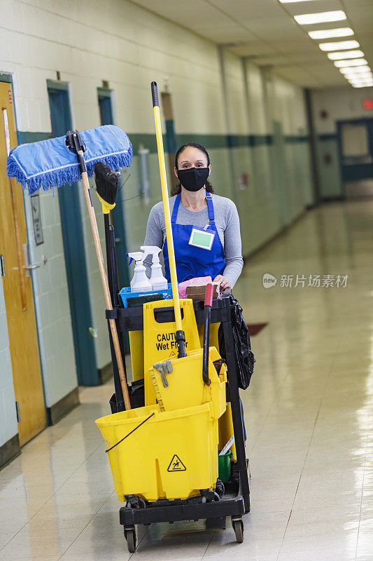 女清洁工在学校走廊推着清洁车，戴着面具