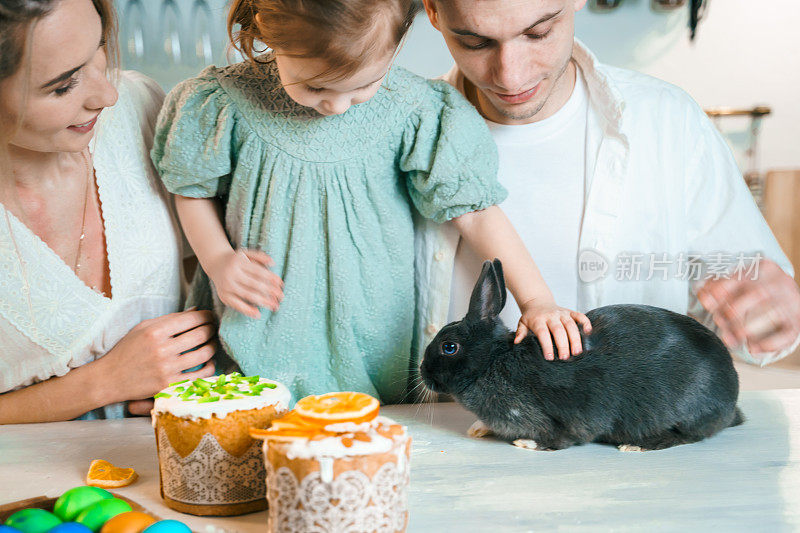 家人，妈妈，爸爸，孩子，女儿庆祝复活节的女孩。烹饪蛋糕，在厨房桌子上画鸡蛋。节日快乐在一起。复活节兔子,兔子
