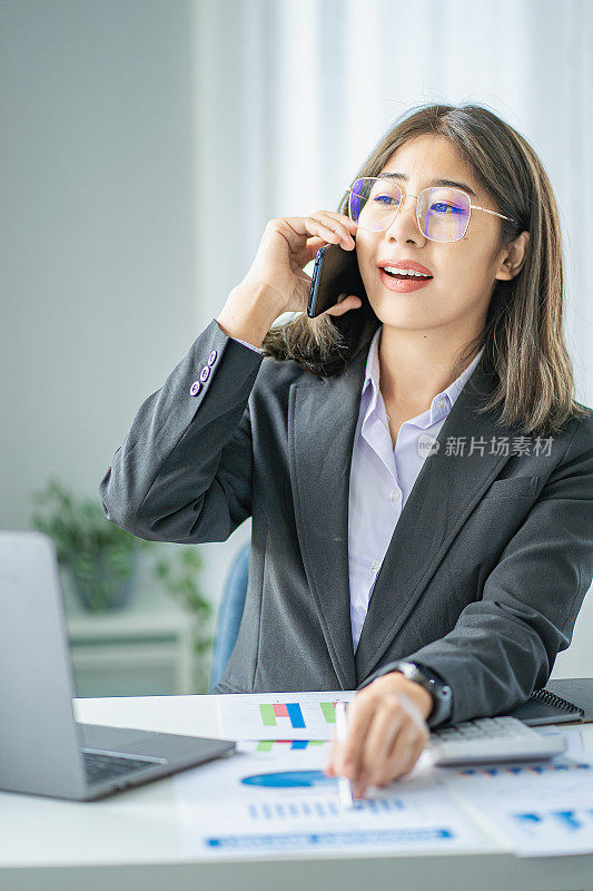 亚洲女商人在办公室用笔记本电脑打电话，做会计，计算，分析财务。