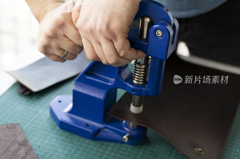 工匠使用手压机在皮革上设置夹子，使钱包。手压扣压机是皮革车间工匠使用的。