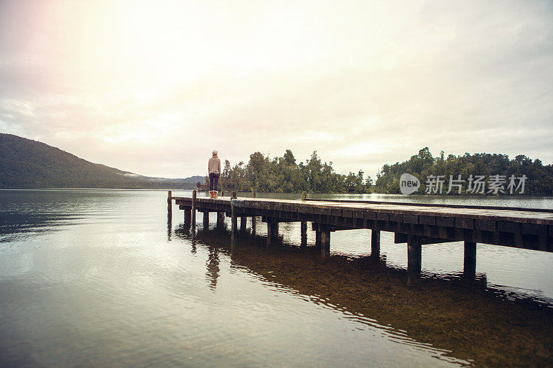 孤身一人的女子站在湖码头上观看壮观的风景