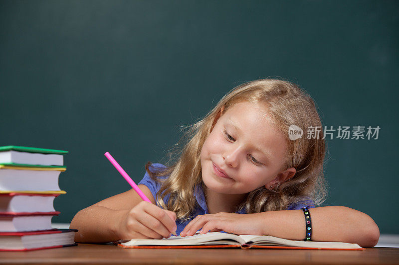 可爱的小女生在黑板前的课桌上写字