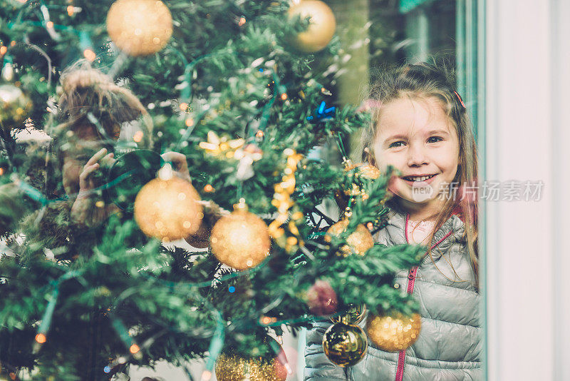 快乐的四岁女孩透过窗户偷看，圣诞树，欧洲