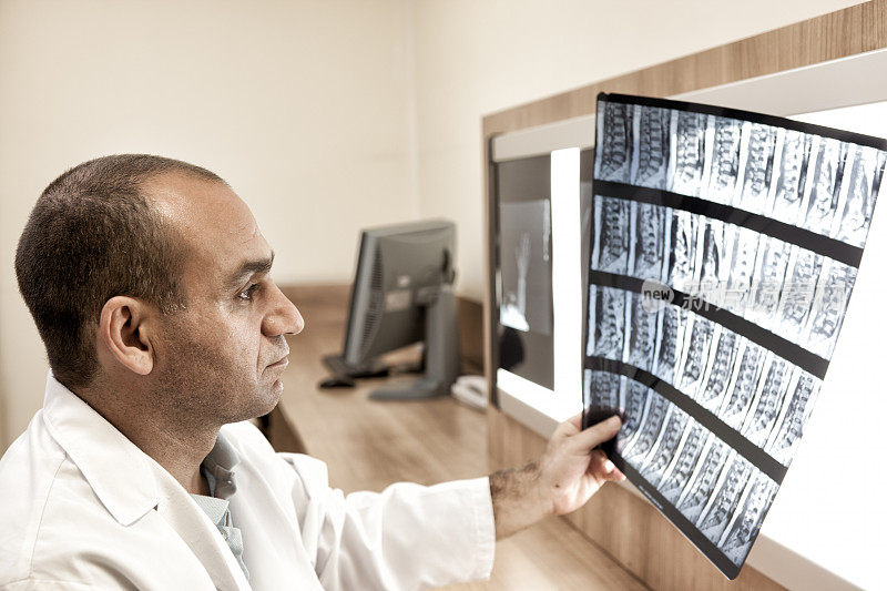 一名男医生正在办公室的亮屏上看核磁共振扫描。