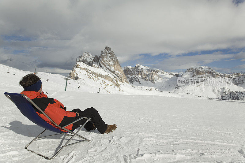 在Dolomites，一个男人坐在折叠椅上看着滑雪坡道