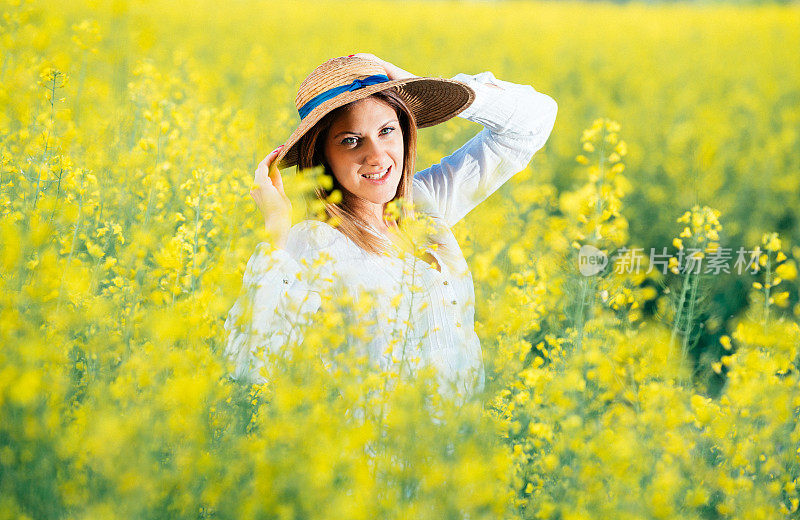 迷人的女人戴着草帽在黄色的田野在夏天