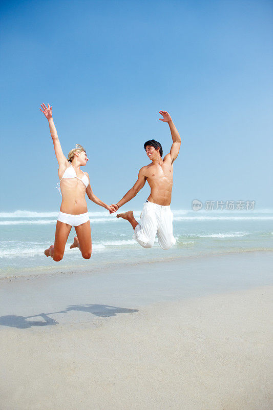 年轻夫妇手牵着手，在海滩上蹦蹦跳跳