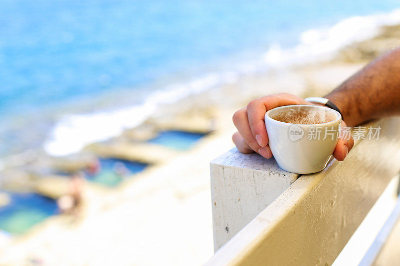 在海滩阳台上拿着咖啡杯的男人