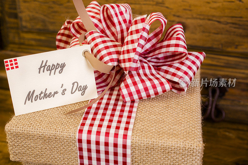 母亲节快乐。棕麻布礼盒，红蝴蝶结，贺卡。