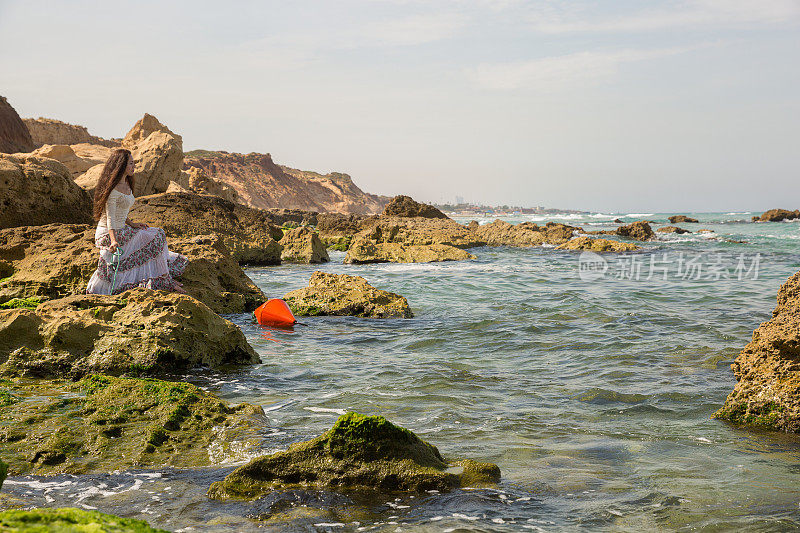坐在海边岩石边沉思的女人