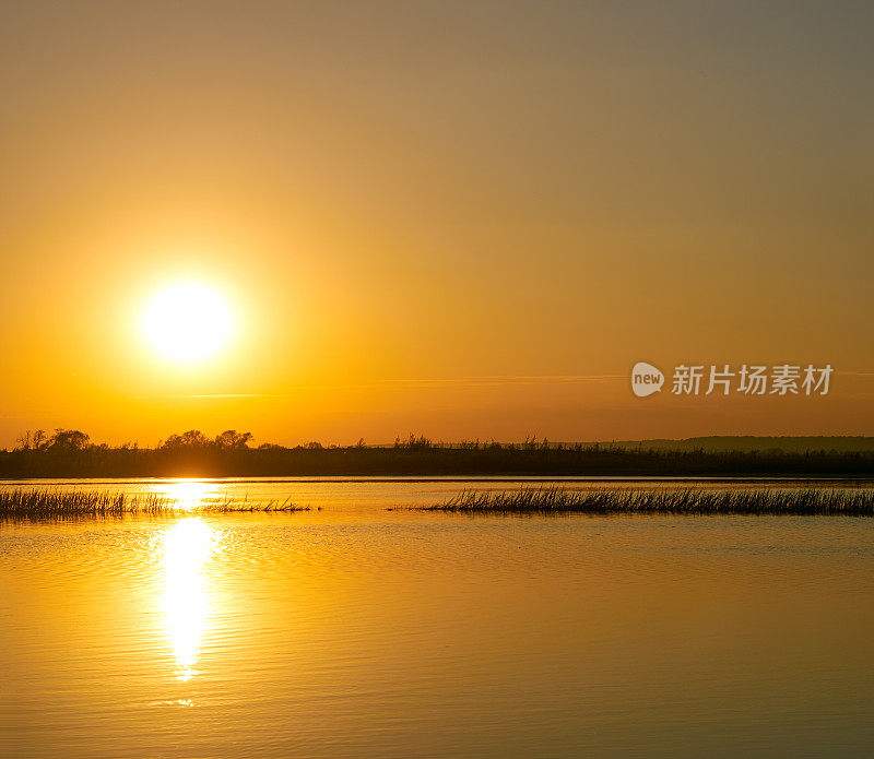 夕阳下的江水，岸边的剪影，天空和太阳倒映在水面上，背光