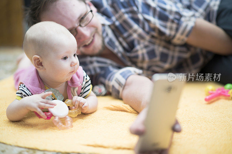一位年轻的父亲和他的小女儿一起躺在地板上，通过手机自拍和视频交谈