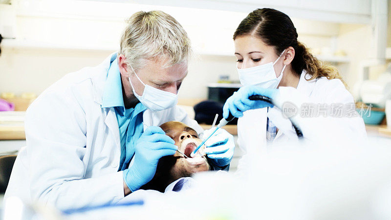 戴着口罩和手套，牙医和助手忙着治疗病人