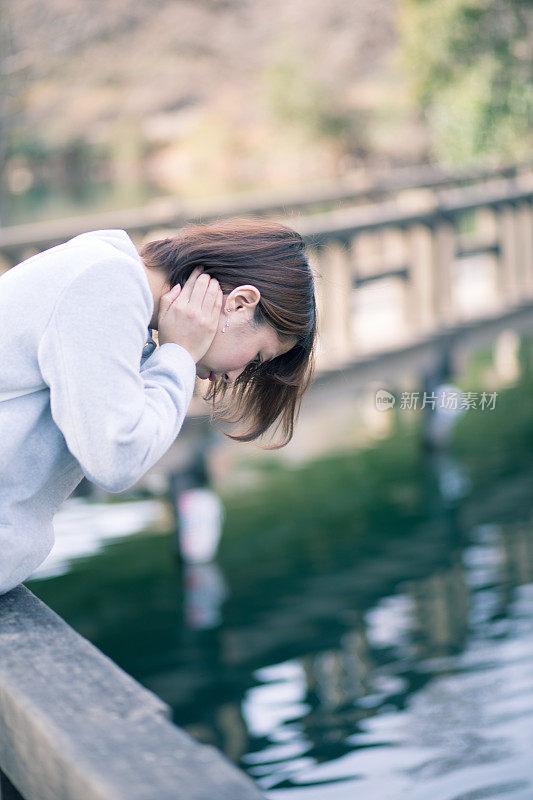 年轻女子从桥上望着池塘