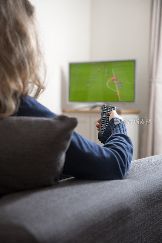 女人坐在沙发上，手里拿着遥控器，在家里的客厅里看电视