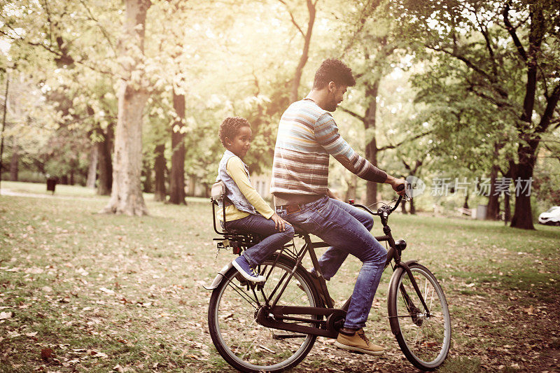 单身非裔美国父亲驾驶他的小女儿在自行车槽公园。