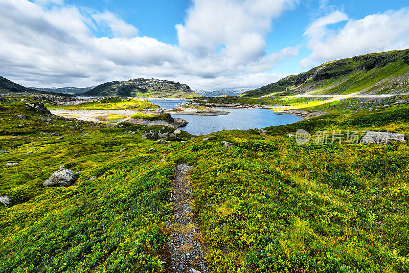 美丽的风景在挪威的高原与绿色的草地，石头，山脉和一个湖与蓝色的云的天空在背景