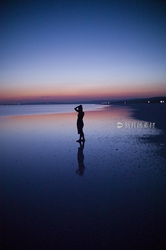 一名女子站在土耳其科尼亚的盐湖上，夕阳西下