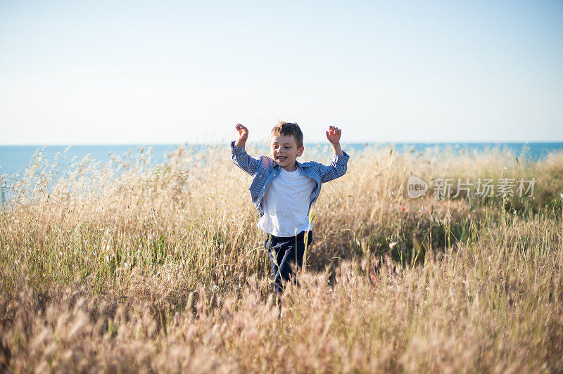 快乐的小男孩奔跑在金色的麦田里，背景是海洋