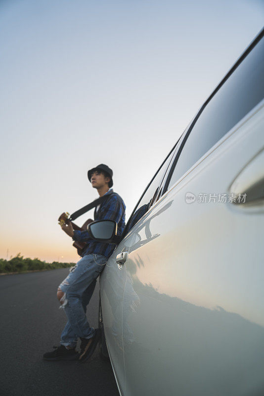 年轻男子靠在汽车引擎盖上弹吉他