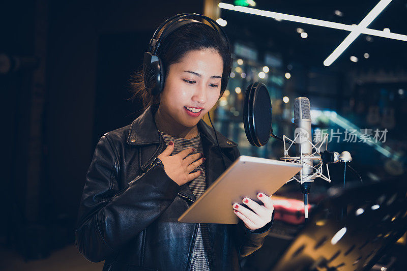 亚洲女孩在录音棚里拿着平板电脑唱歌，中国上海