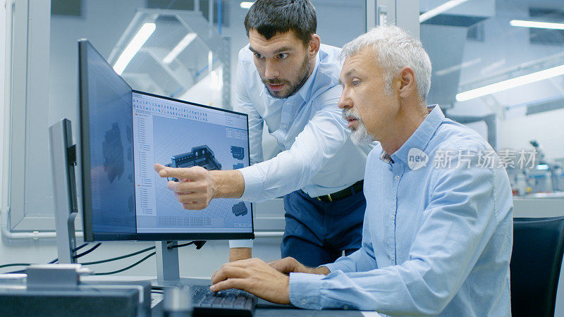 工业设计人员在使用CAD程序，设计新部件时与高级工程师交谈。他从事双显示器个人电脑的研究。