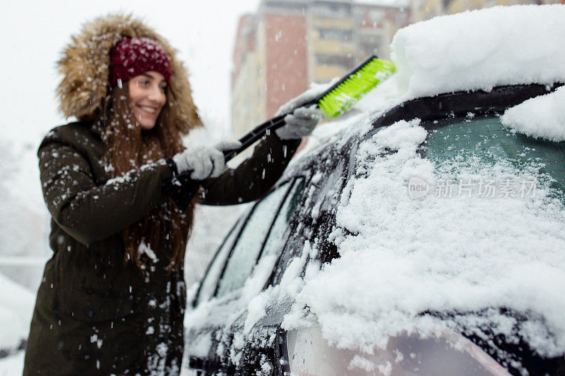 年轻女子在清理车上的积雪