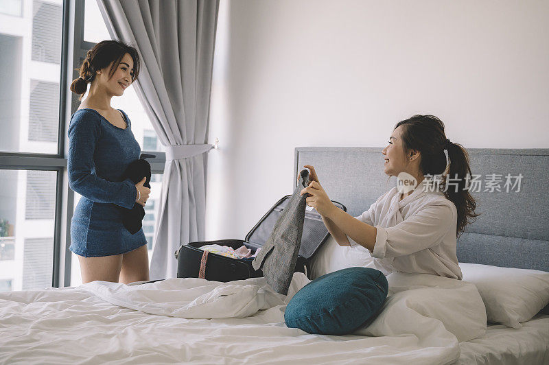 一位亚裔华人女性坐在她的床上给她妹妹看她的新衣服