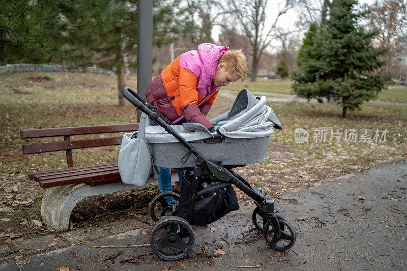 年轻的单身母亲，和她的儿子在公园里，一个坐轮椅的男孩，照顾着，关心着。一个幸福的家庭。在户外散步。母亲节，保护儿童。一个正在散步的小孩。