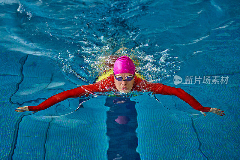 女运动员穿着红黄相间的泳衣在游蛙泳。水花四溅向不同的方向。