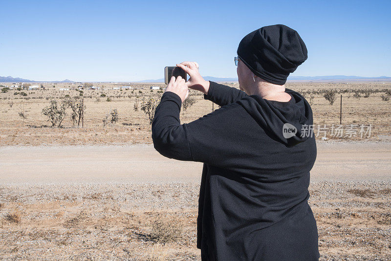 旅行的记忆。一位成熟的女性，一名游客，在新墨西哥州的公路旅行中用智能手机拍下了沙漠的风景